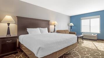 Habitación de hotel con una cama grande, dos lámparas de noche, una mesita, una silla y una ventana con persianas.