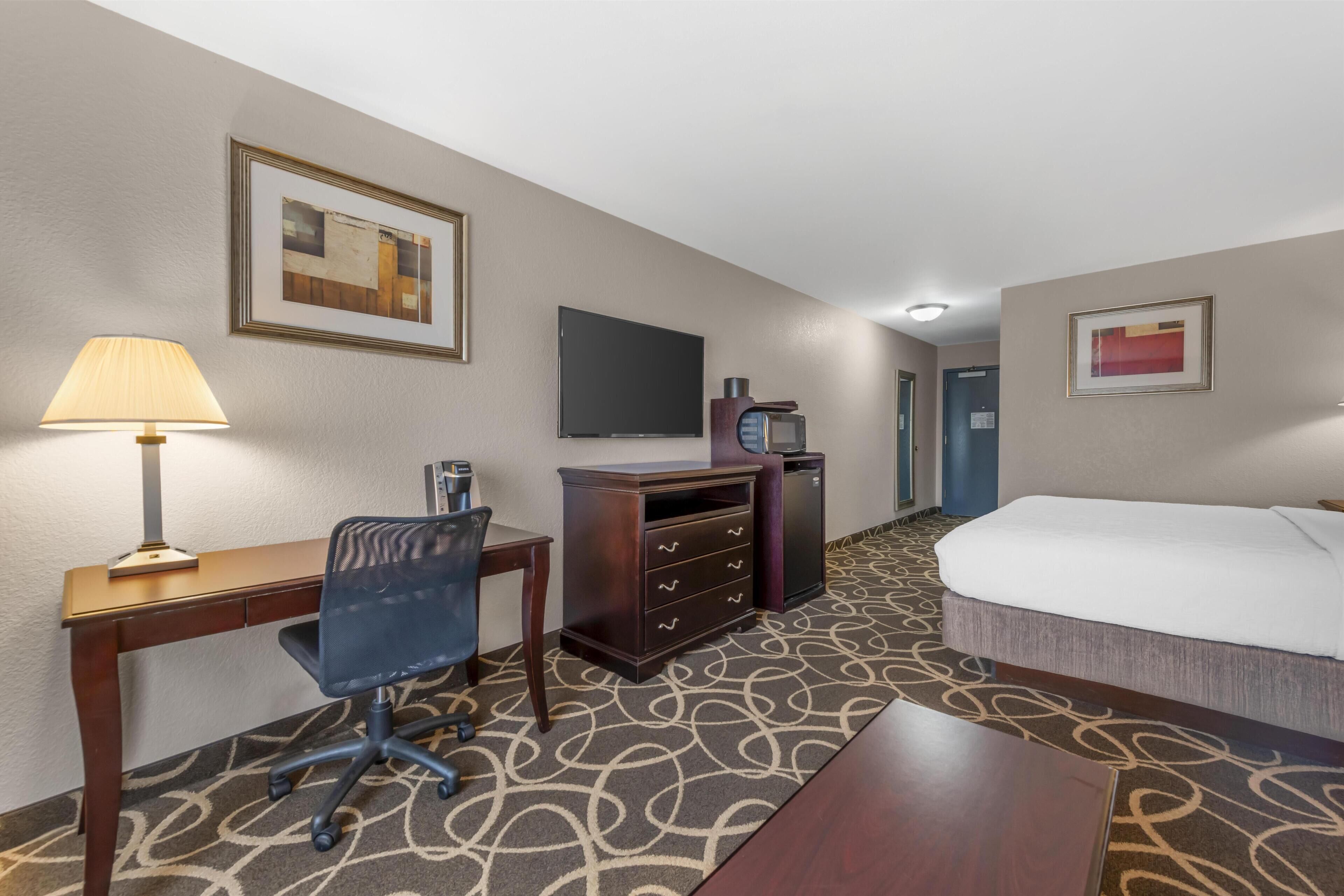 Habitación de hotel con escritorio, silla, cómoda, televisor y cama.