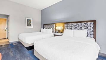 Quarto de hotel com duas camas, uma mesa de cabeceira, um abajur e um quadro na parede.
