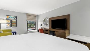Quarto de hotel moderno com uma cama grande, uma escrivaninha com televisão de tela plana, uma janela com persianas e obras de arte na parede.