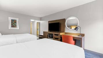Habitación de hotel con dos camas, un escritorio, un televisor de pantalla plana, un microondas, un espejo redondo y un cuadro en la pared.