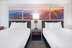 A hotel room with two beds, a nightstand with a lamp, and a large landscape painting above the beds. - Days Inn by Wyndham Hamilton (Hamilton)