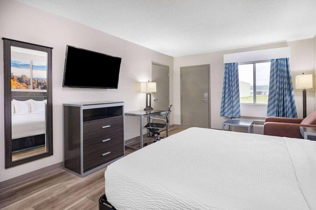 A hotel room with a large bed, a desk, a chair, a TV, and a window with curtains.