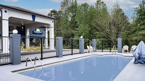 A pool area with a clear blue pool, a covered seating area, and a building with a 'Days Inn & Suites' sign. - Days Inn by Wyndham Hamilton (Hamilton)