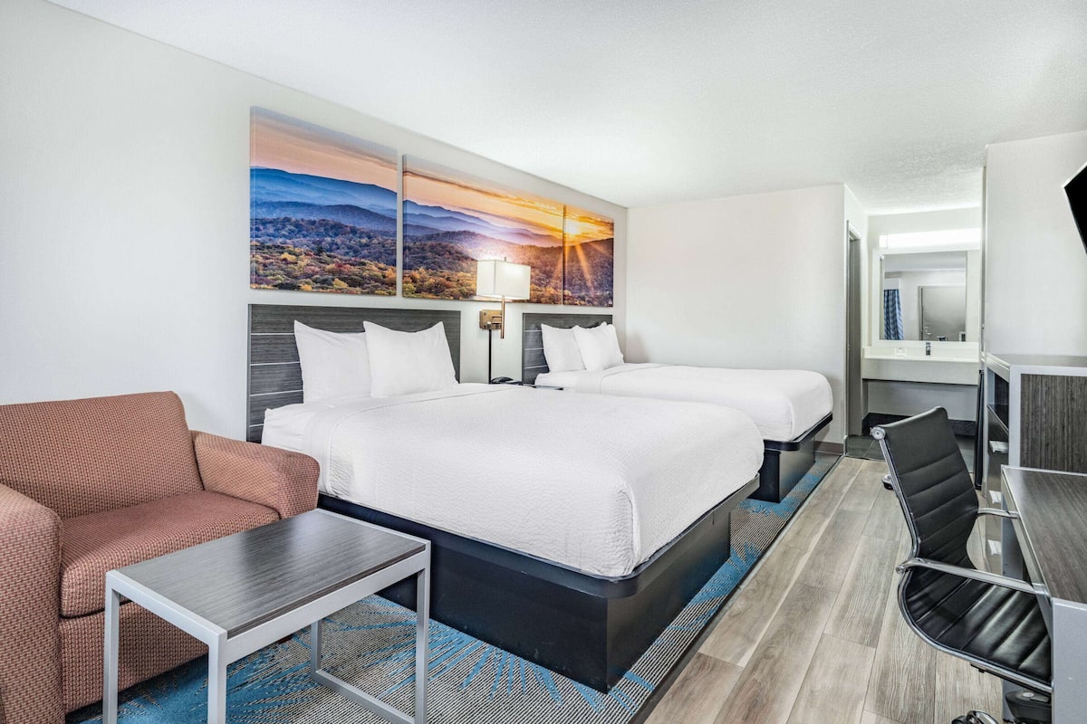 A hotel room with a large bed, two smaller beds, a sofa, a desk, and a chair.