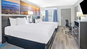 A hotel room with a large bed, two bedside tables with lamps, a desk with a chair, a television, and a window with curtains.