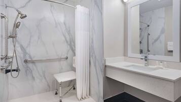 Un baño moderno con ducha a nivel, un banco, un espejo grande y un lavamanos blanco.
