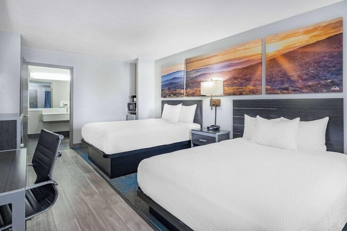 A hotel room with two beds, a desk, a chair, a TV, and a painting on the wall.