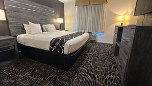 Quarto de hotel com uma cama grande, mesas de cabeceira, televisão de tela plana e uma janela ampla com cortinas.