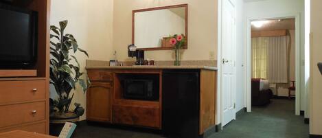 Habitación de hotel con escritorio de madera, televisor, microondas, lavamanos y espejo.