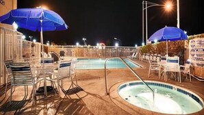 Uma área de piscina com espreguiçadeiras, guarda-sóis e uma banheira de hidromassagem.