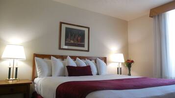 A hotel room with a large bed, two bedside tables with lamps, a framed picture on the wall, and a window with curtains.