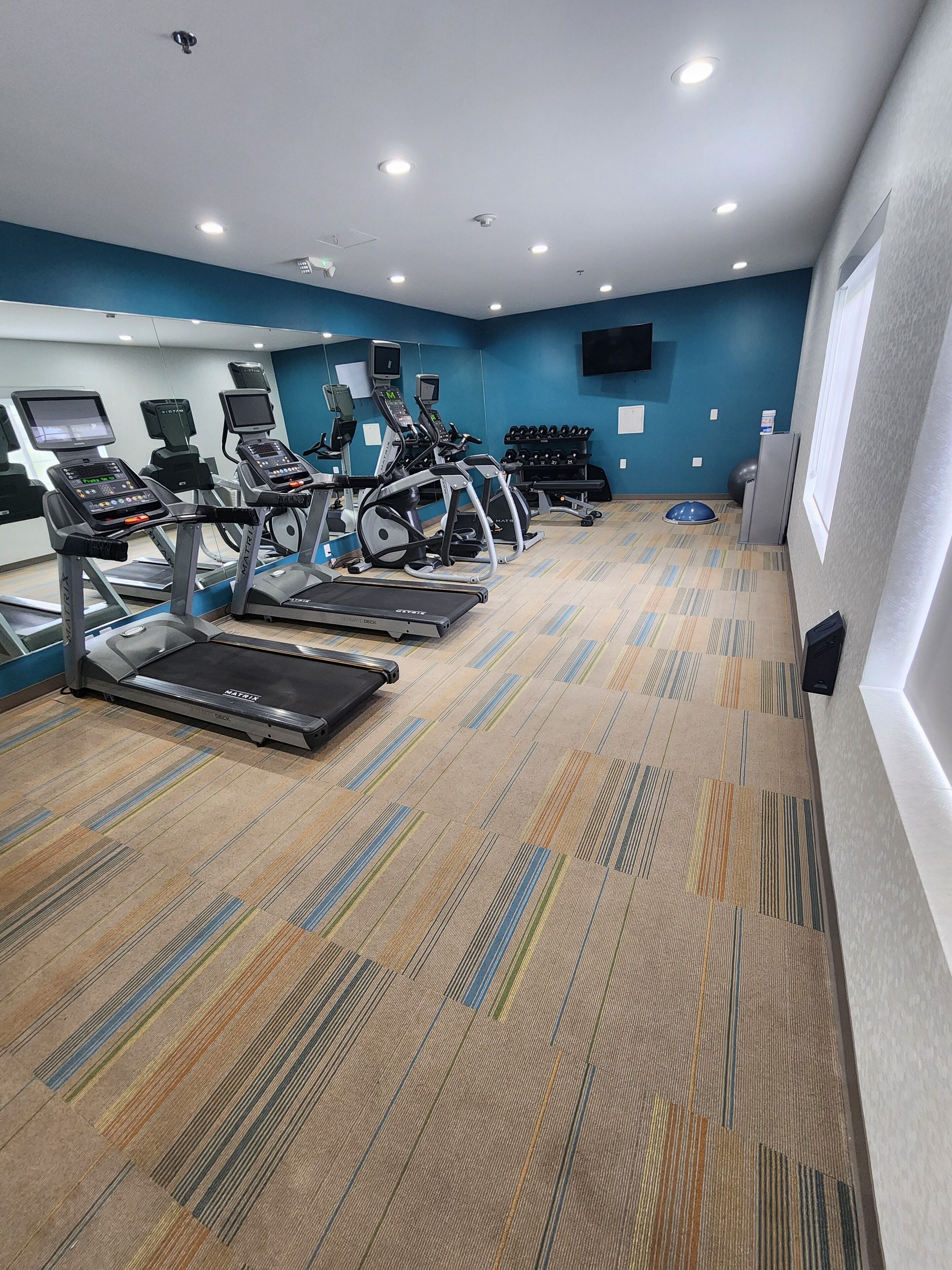 A gym with treadmills, elliptical machines, and a weight bench.