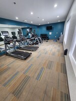 Un gimnasio con cintas de correr, elípticas y una banca para pesas.