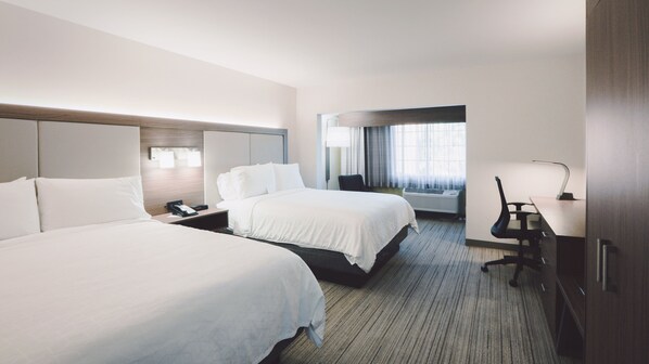 A hotel room with two beds, a desk, a chair, and a window with curtains.