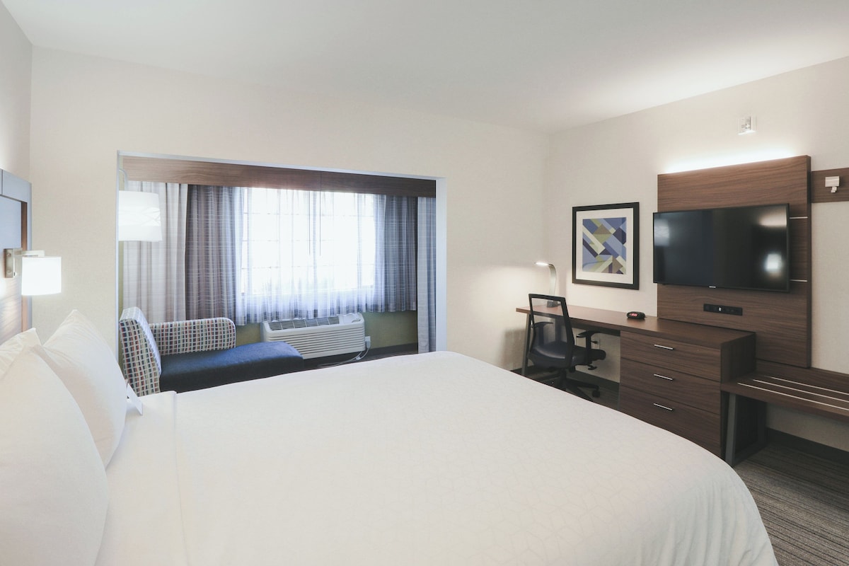 A hotel room with a large bed, a desk, a chair, a television, and a window with curtains.