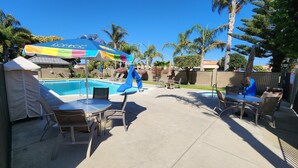 A backyard with a swimming pool, patio furniture, and a colorful umbrella.