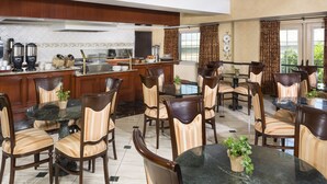 A spacious dining area with multiple round tables and chairs, a kitchen with modern appliances, and large windows providing natural light. - Ayres Suites Ontario at the Mills Mall - Rancho Cucamonga (Ontario)