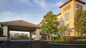 A hotel with a covered entrance, a prominent sign reading "AYRES SUITES," and a well-maintained landscaped area with trees and shrubs. - Ayres Suites Ontario at the Mills Mall - Rancho Cucamonga (Ontario)