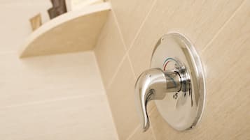 A bathroom with a wall-mounted faucet, a shelf with toiletries, and a tiled wall.
