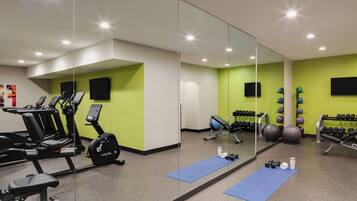 A gym with exercise equipment, a mirror, and a green wall.