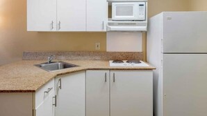 A kitchen with white cabinets, a microwave, a refrigerator, and a granite countertop. - Extended Hotel Studio (San Dimas)