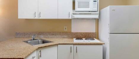 A kitchen with white cabinets, a microwave, a refrigerator, and a granite countertop.