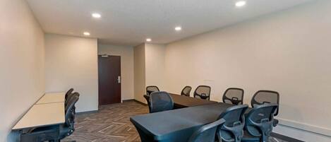 A conference room with a large table and multiple chairs, carpeted floor, and recessed ceiling lights.