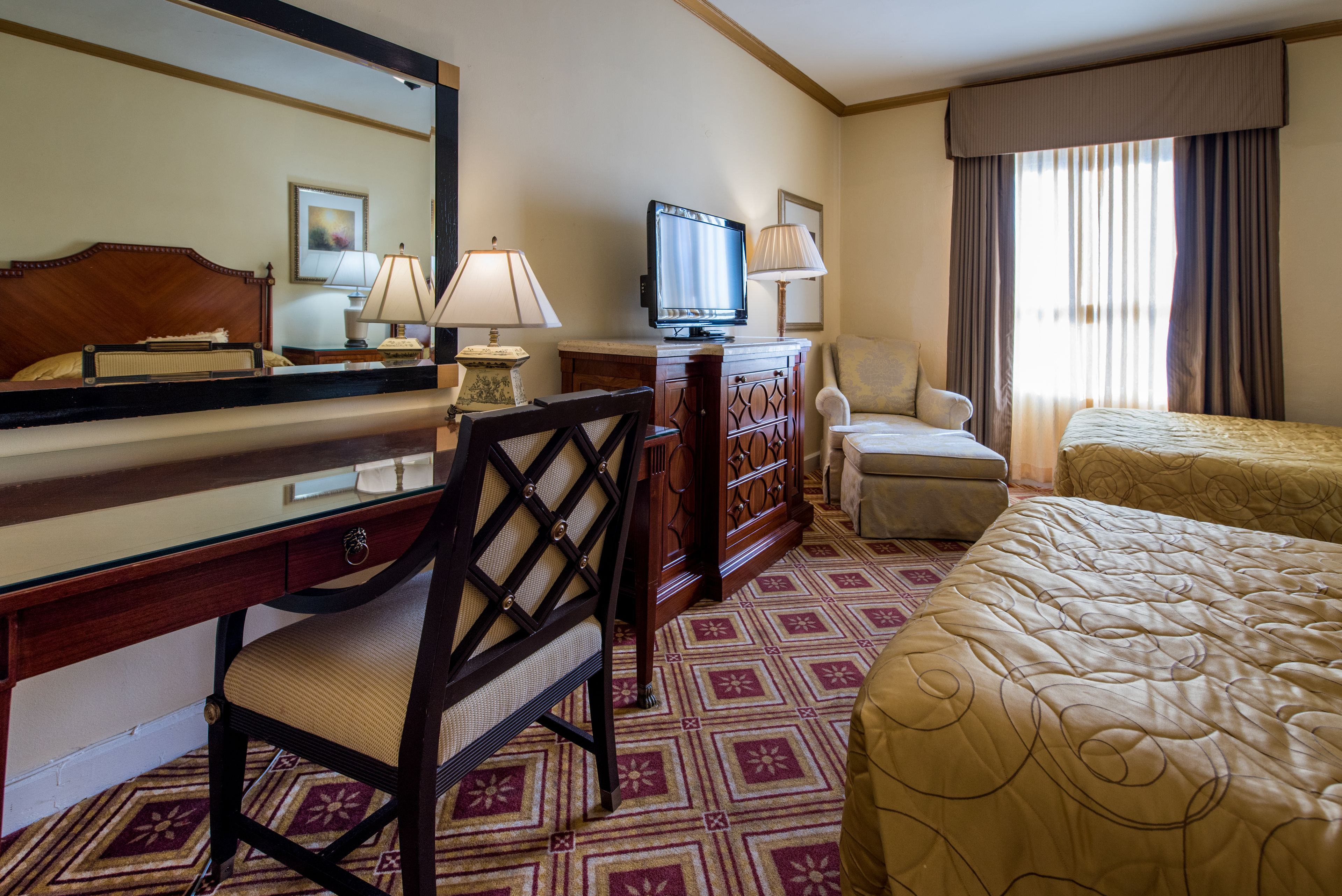 A hotel room with a bed, a desk with a chair, a television, and a large mirror.