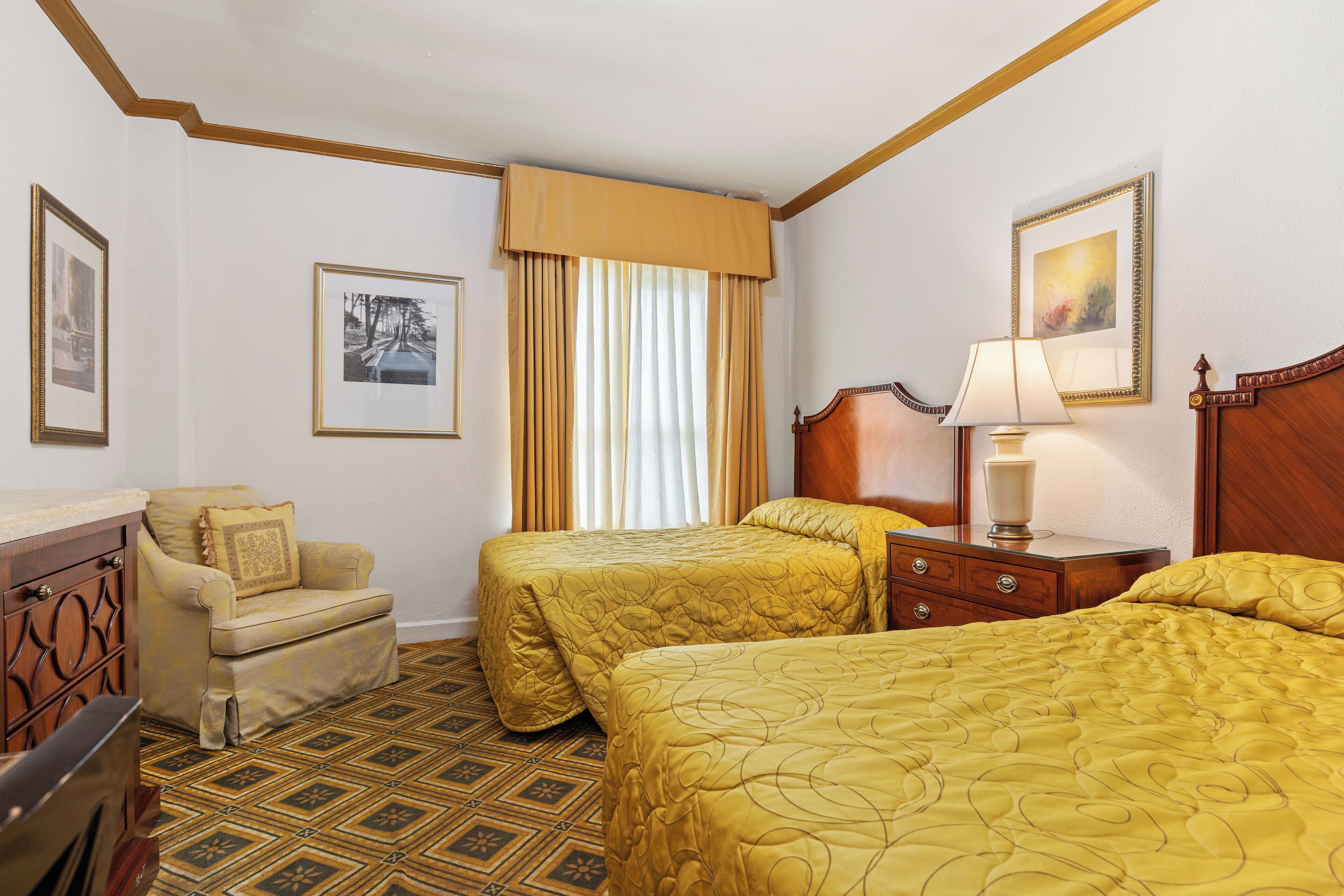 A hotel room with two beds, a chair, a dresser, and a window with curtains.