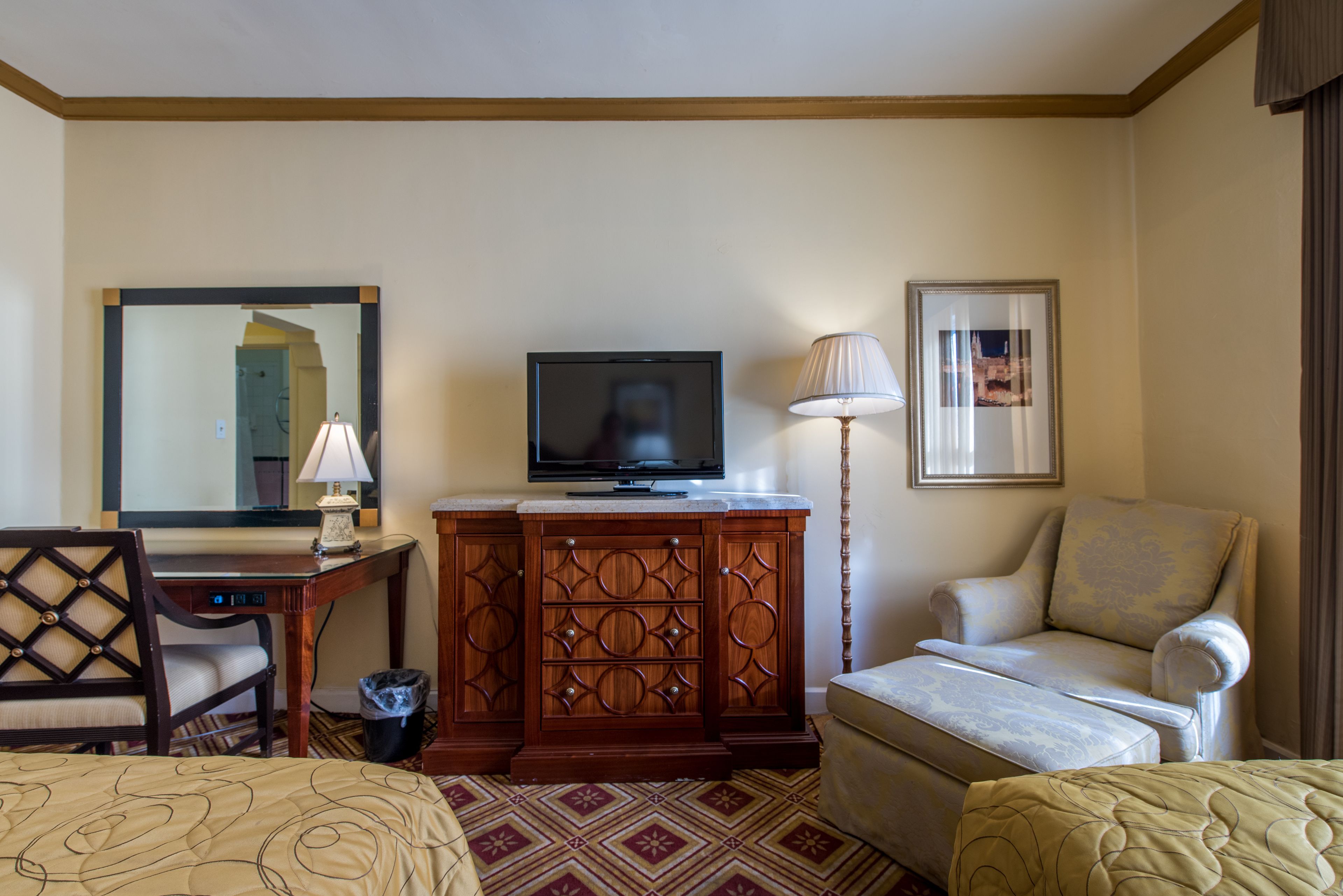 A hotel room with a bed, a desk with a lamp, a television, a chair, and a cabinet.