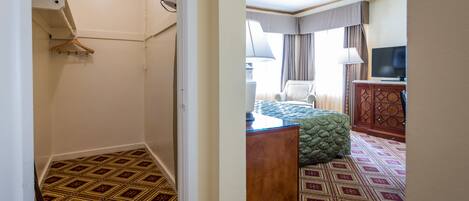 A hotel room with a patterned carpet, a bed with a green quilt, a wooden dresser, a television, and a window with curtains.