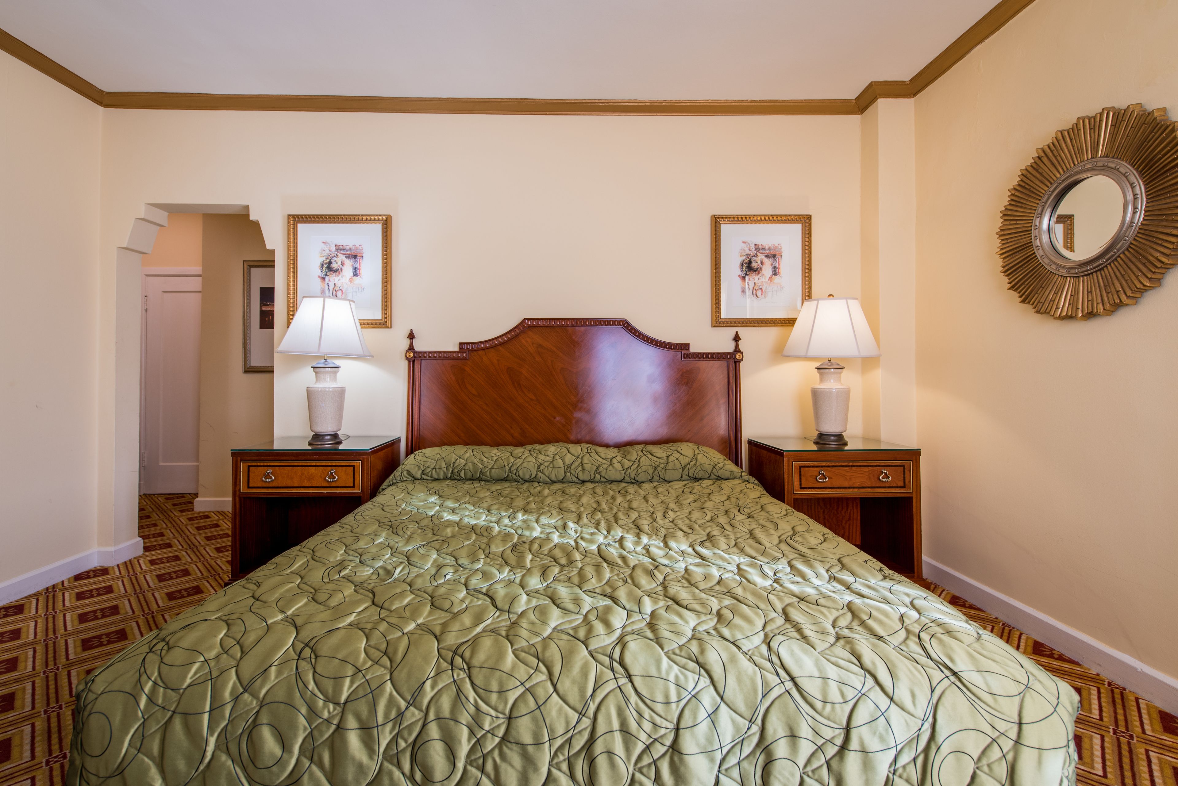 Une chambre d’hôtel avec un grand lit, deux tables de chevet avec des lampes, une tête de lit en bois et deux tableaux encadrés accrochés aux murs.