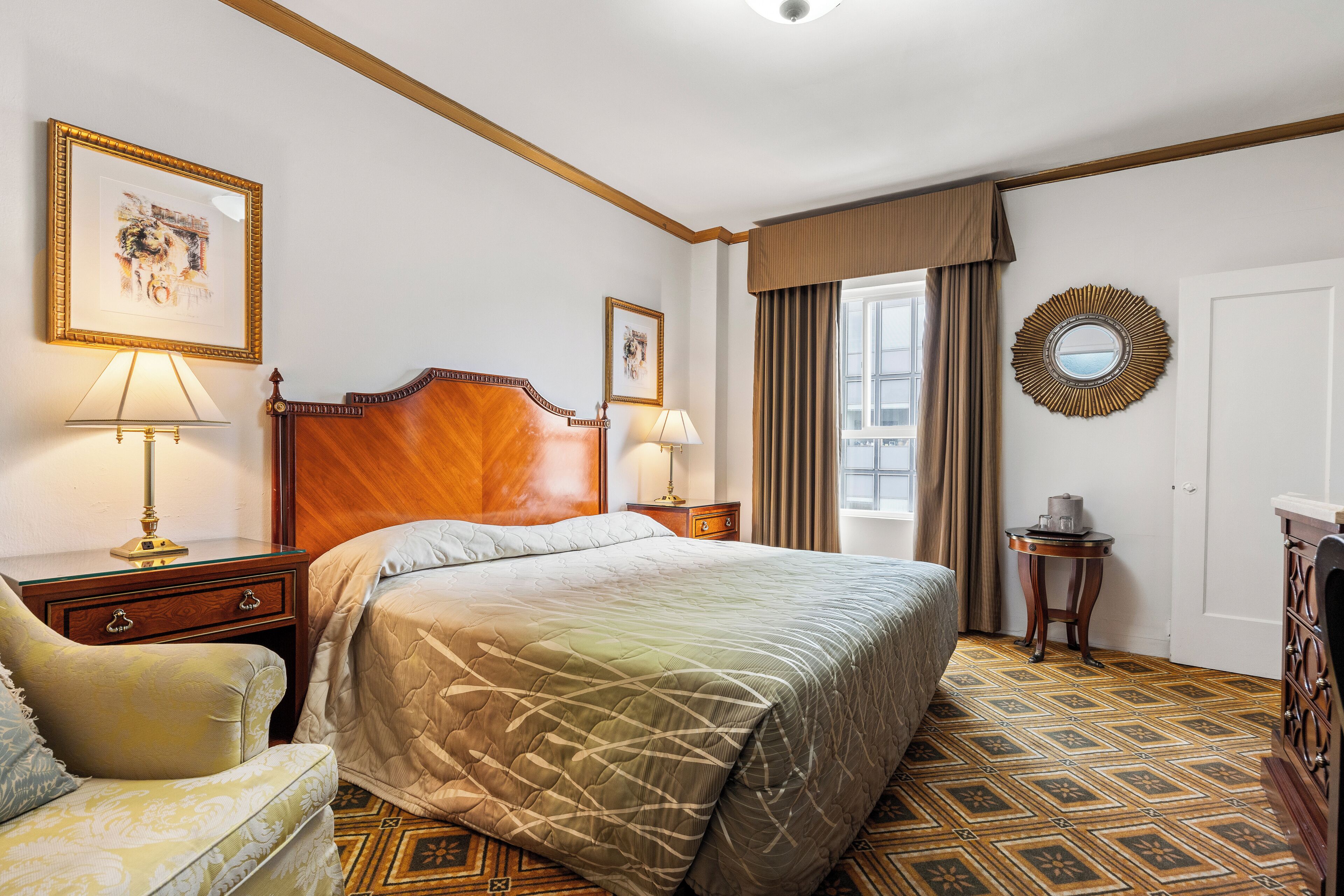 A hotel room with a large bed, two bedside tables with lamps, a chair, a dresser, and a mirror on the wall.