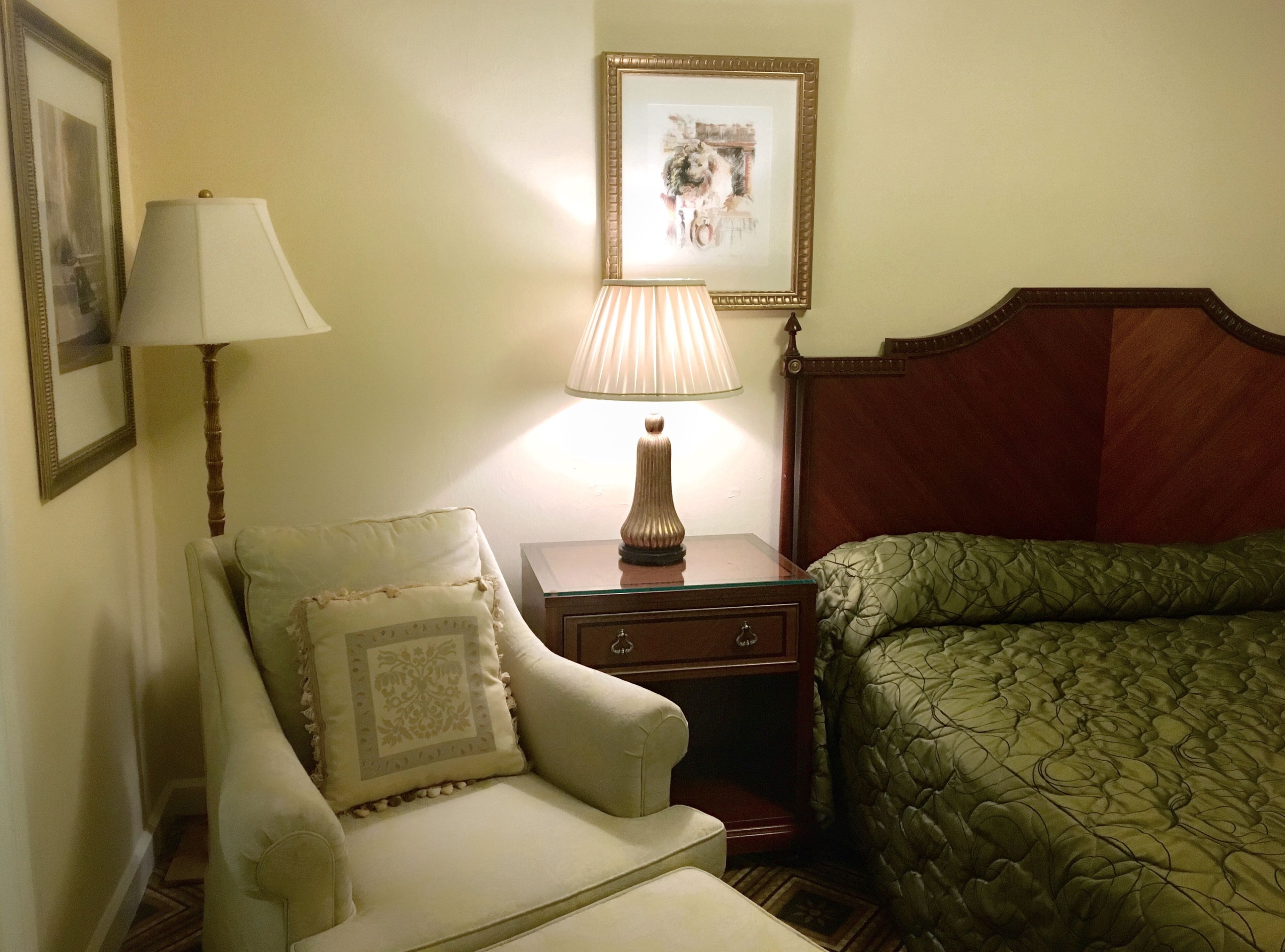 Habitació d'hotel amb un llit, una cadira, una taula de nit, una làmpada i un quadre al mur.