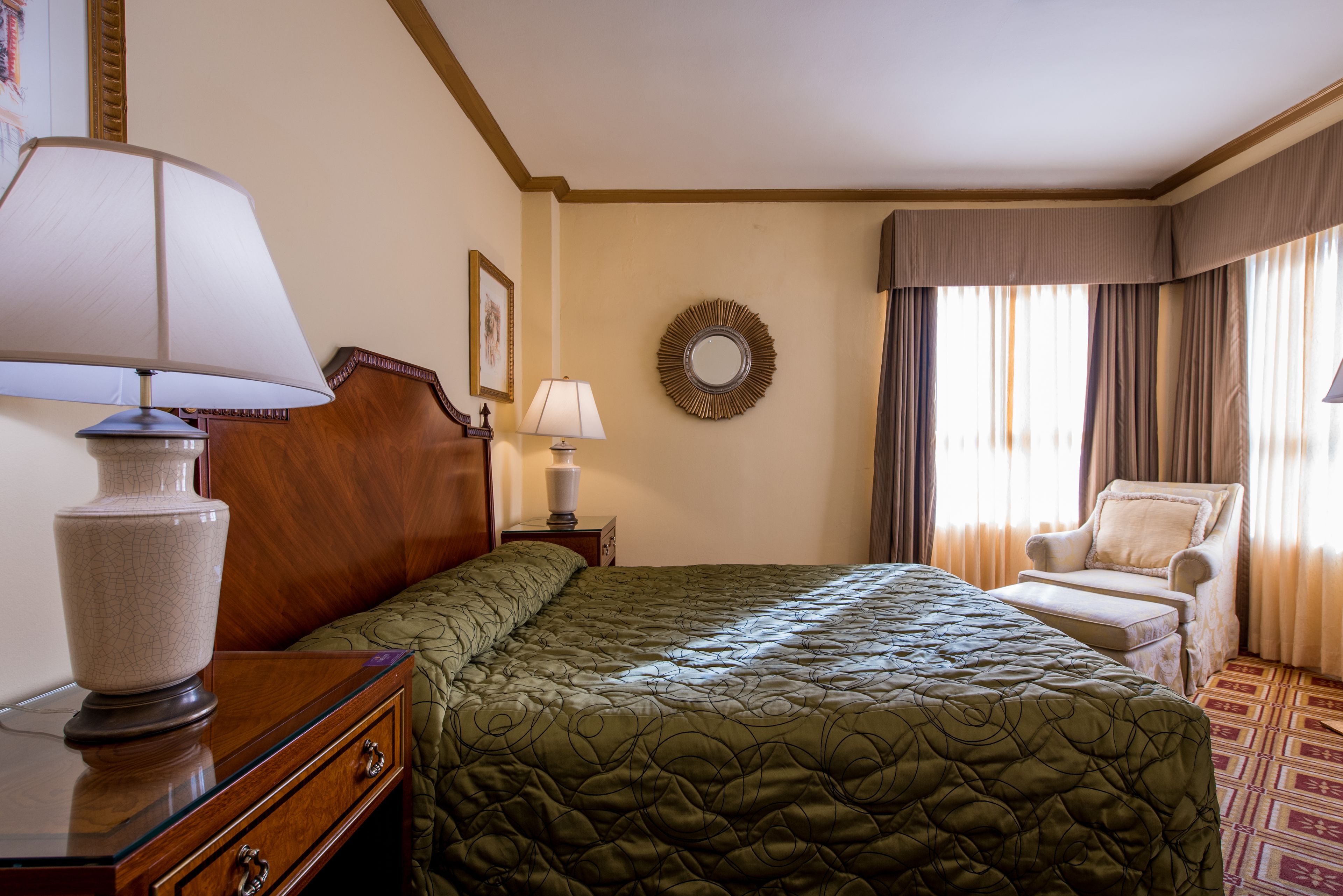A hotel room with a large bed, a wooden nightstand, a lamp, a chair, and a window with curtains.