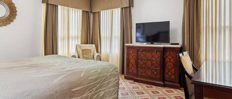 A hotel room with a large bed, a wooden cabinet with a flat-screen TV, a chair, and curtains.