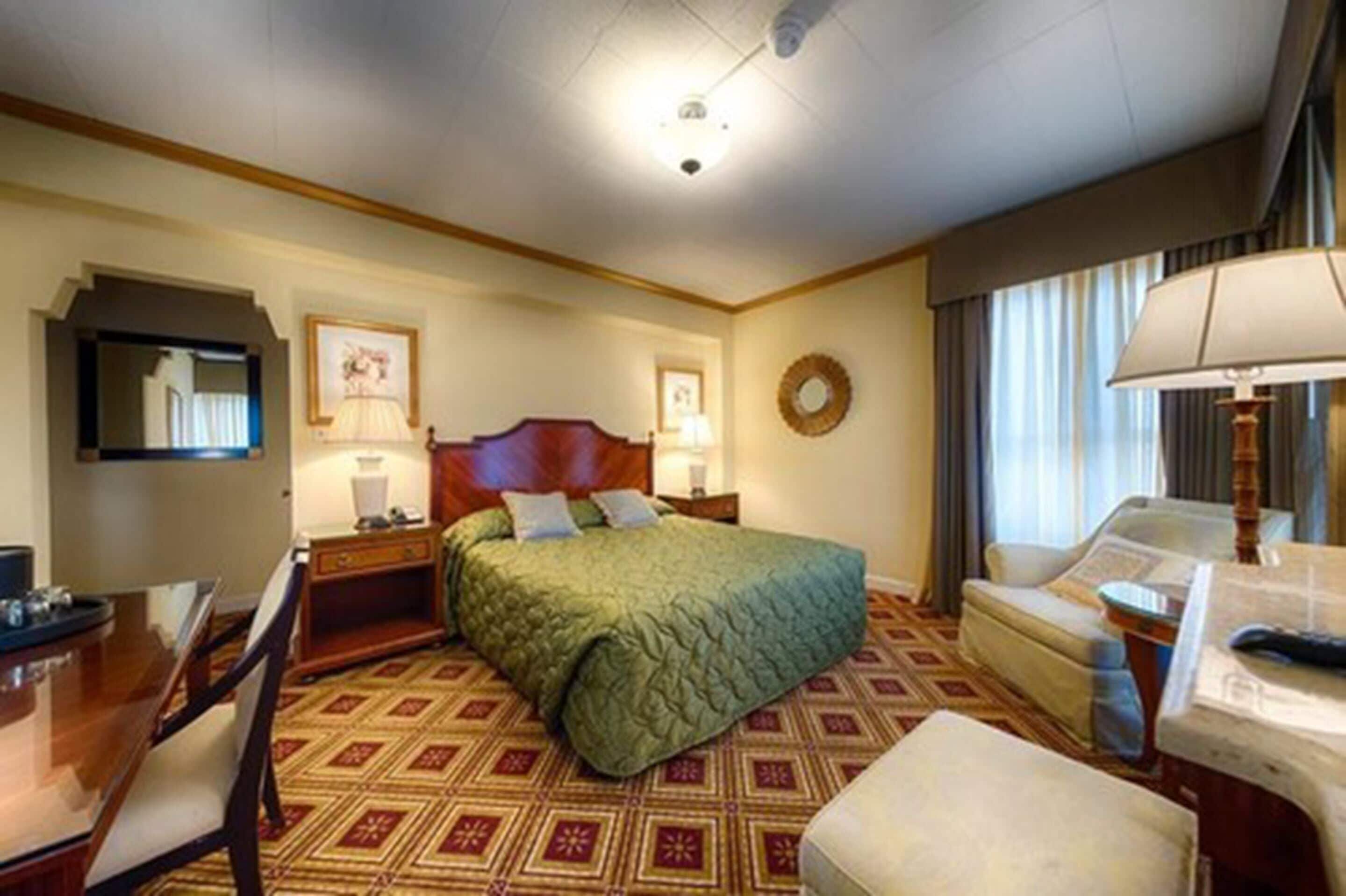 A hotel room with a bed, a desk, a chair, and a sofa.
