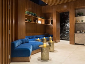 A modern interior with a blue sofa, round tables with candles, wooden shelving with plants, and a wall mural.