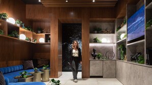 Un interior moderno con un sofá azul, estanterías de madera con plantas y un cuadro grande en la pared.