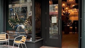 Un café con diseño moderno, que cuenta con un escaparate de vidrio y un área de estar con sillas afuera.
