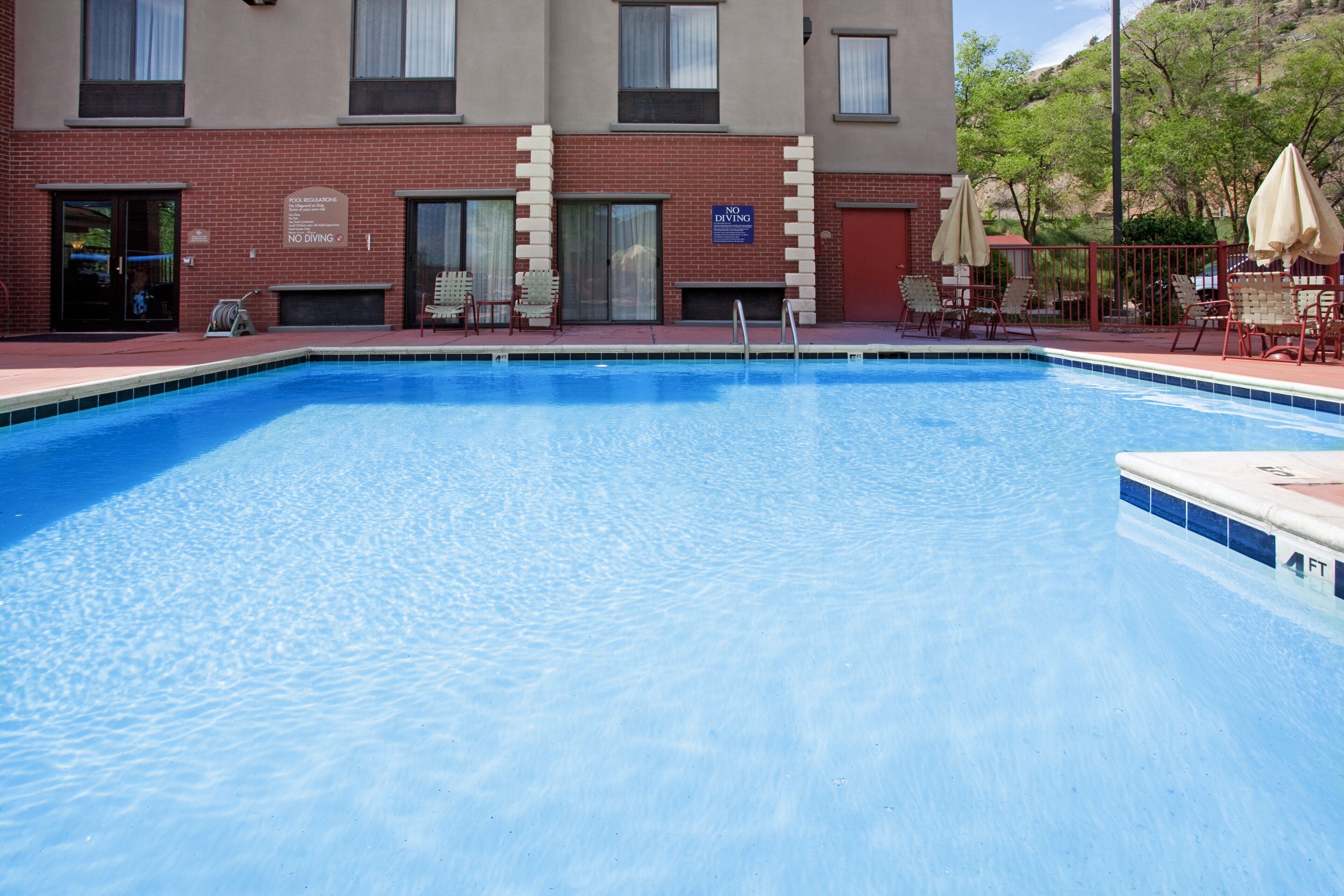 A swimming pool with a no diving sign, outdoor seating, and a building with a brick facade.