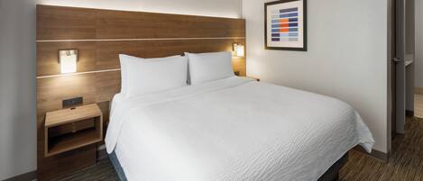 Una habitación de hotel con una cama grande, mesitas de noche, una lámpara de pared e imagen enmarcadas.