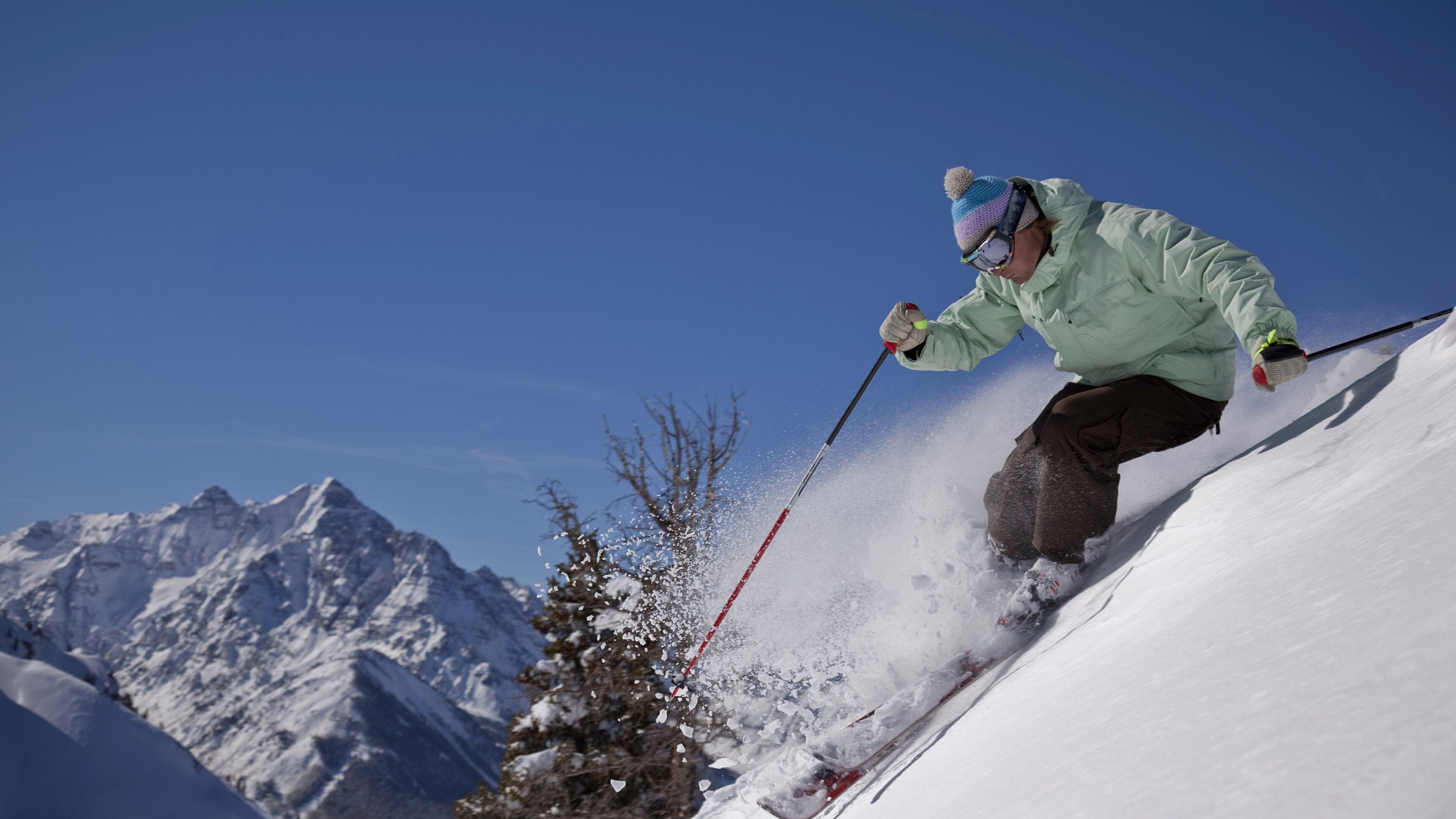 A person skiing down a snowy slope with a clear sky and mountains in the background.