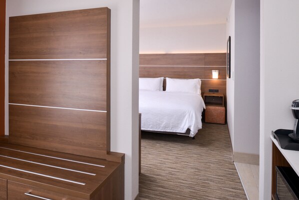 A hotel room with a wooden headboard, a bed with white bedding, a nightstand with a lamp, and a small seating area with a bench. - Holiday Inn Express Glenwood Springs by IHG (Glenwood Springs)