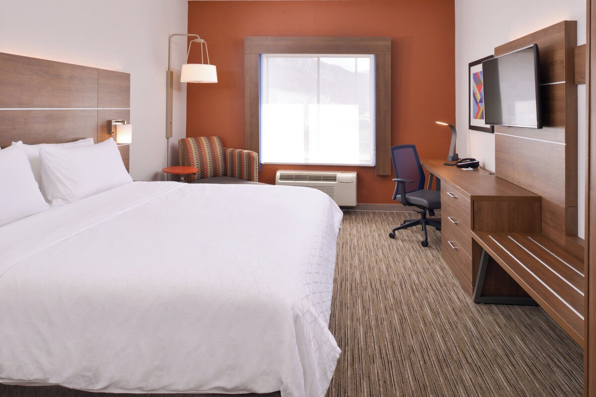 A hotel room with a large bed, a desk, a chair, a television, and a window.