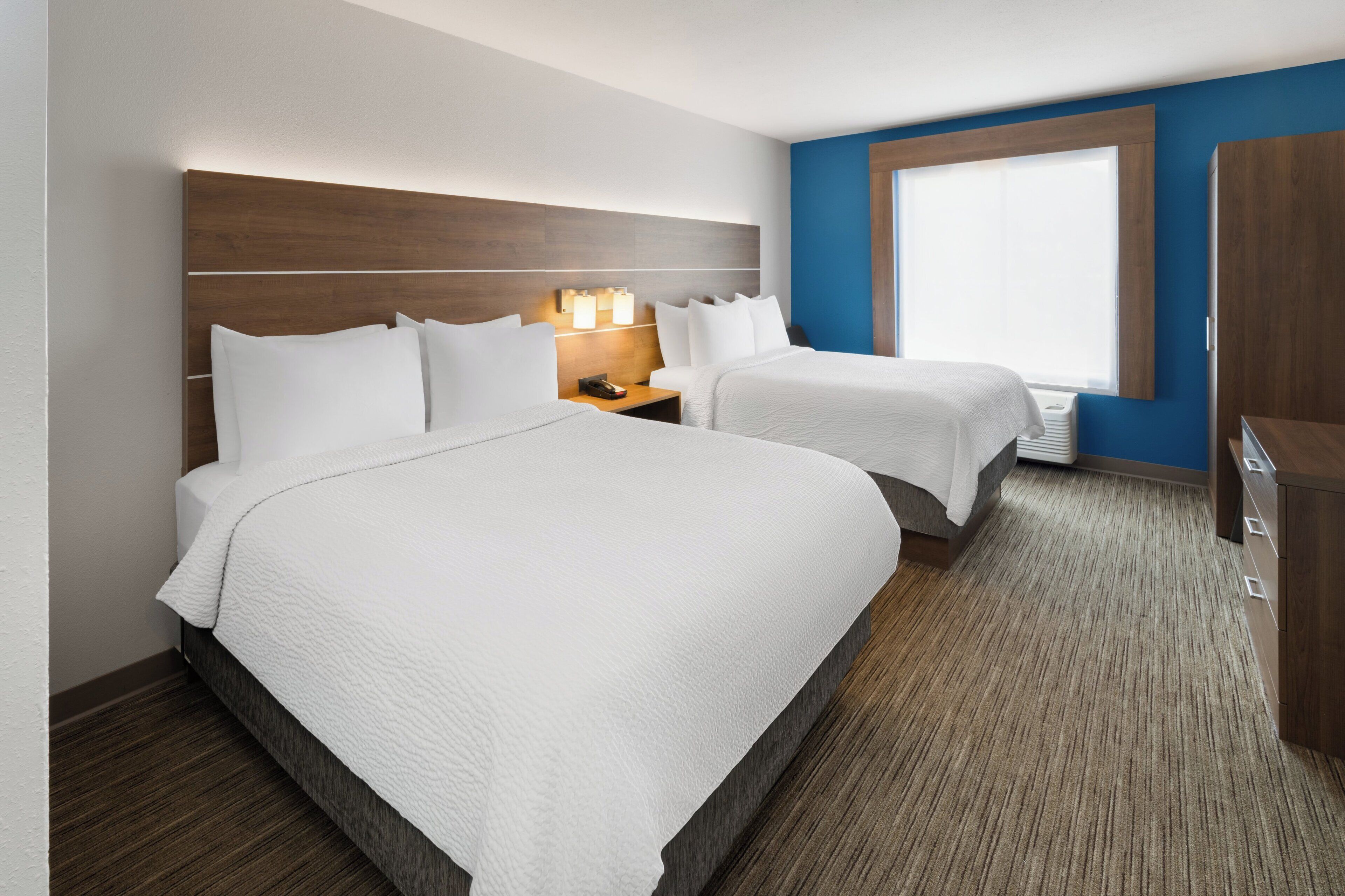 A hotel room with a large bed, a smaller bed, a nightstand with a lamp, and a wardrobe.
