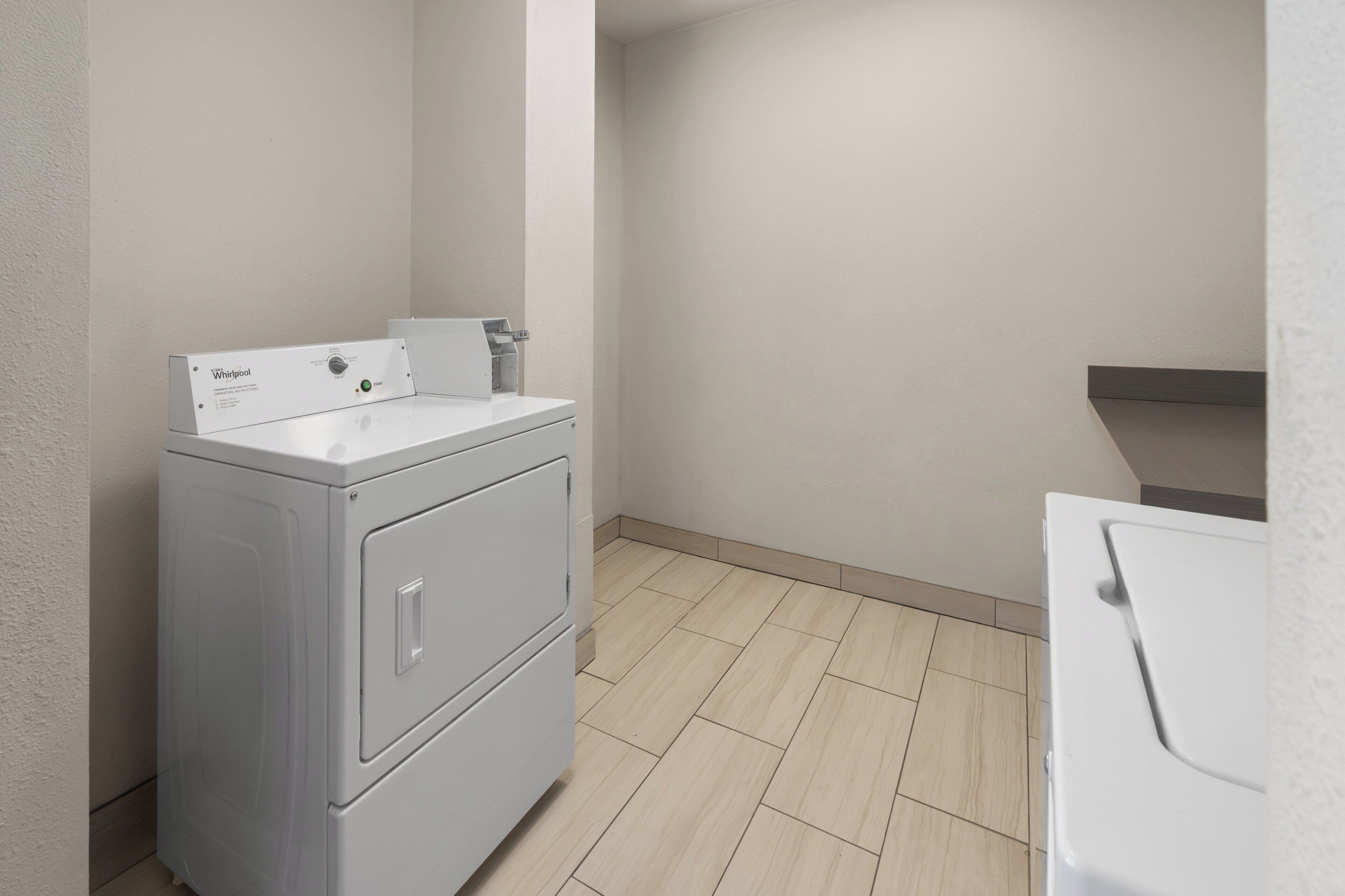 A laundry room with a front-loading washer and dryer, a control panel, and a tiled floor.