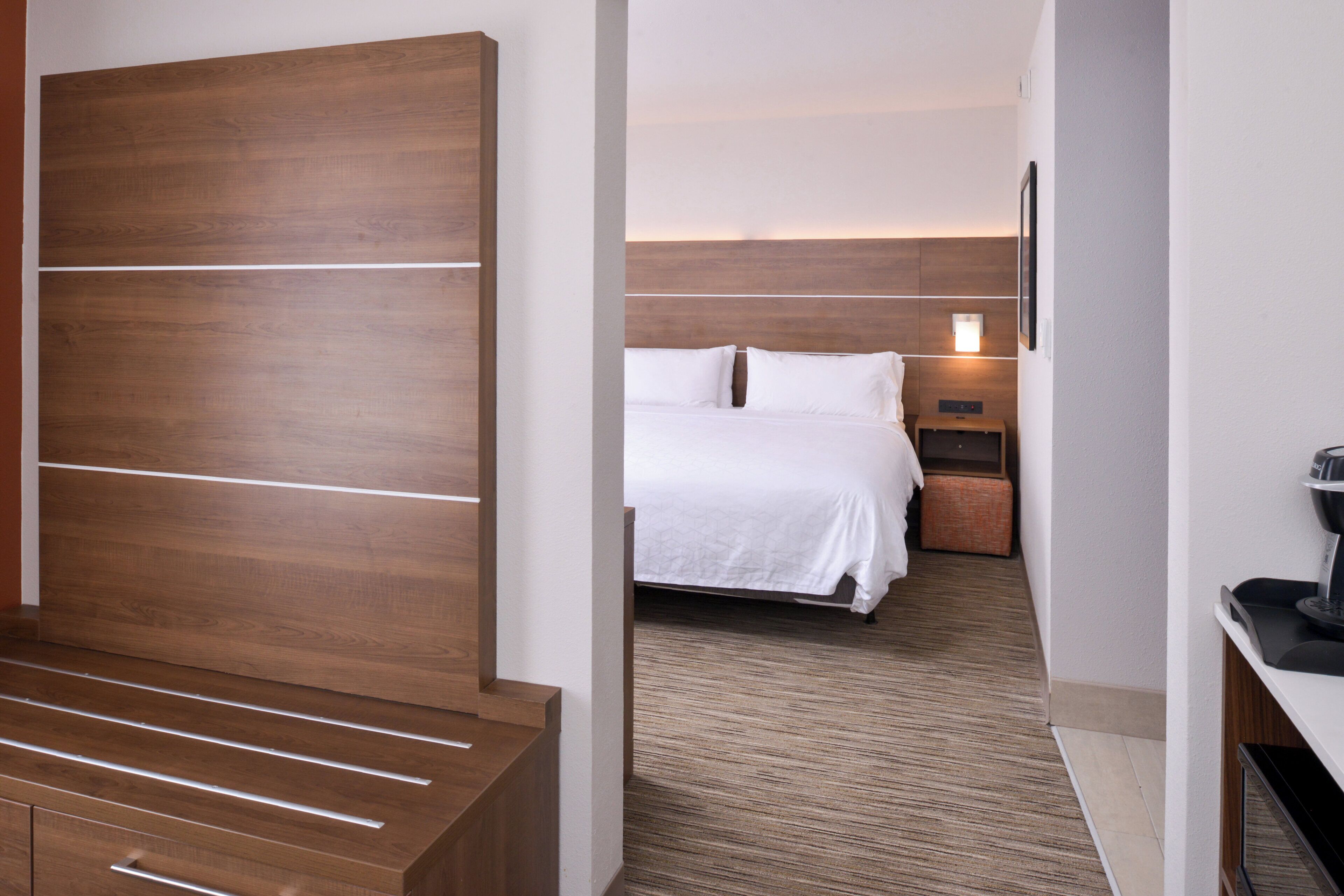 A hotel room with a wooden headboard, a bed with white bedding, a nightstand, and a coffee machine.