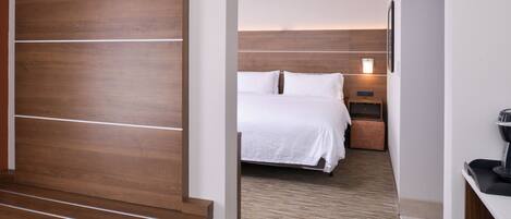 A hotel room with a wooden headboard, a bed with white bedding, a nightstand, and a coffee machine.